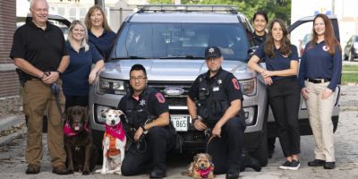 REACH team in 2021: from left Lt. Tim Hetrick with therapy K9 Winston, Crisis Responder Amanda Brockway, Crisis Responder Becky Rowe, Officer Alex Tran with therapy K9 Lollipop, Officer Michael Mitrou with therapy K9 Rosie, Officer Elma Halpin, Crisis Outreach Coordinator Megan Cambron and Behavioral Health Detective Beth Visel